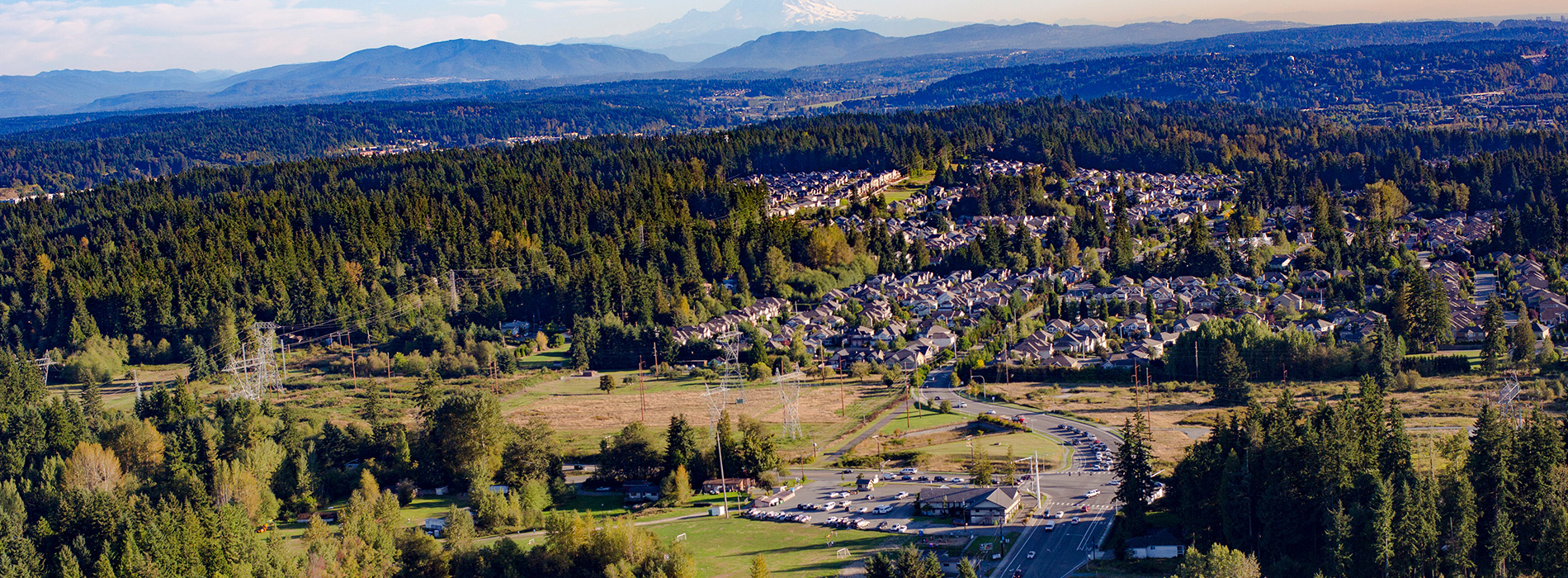 The image displays a panoramic view of a suburban area with houses and trees under a clear sky, featuring a mountain range in the distance.