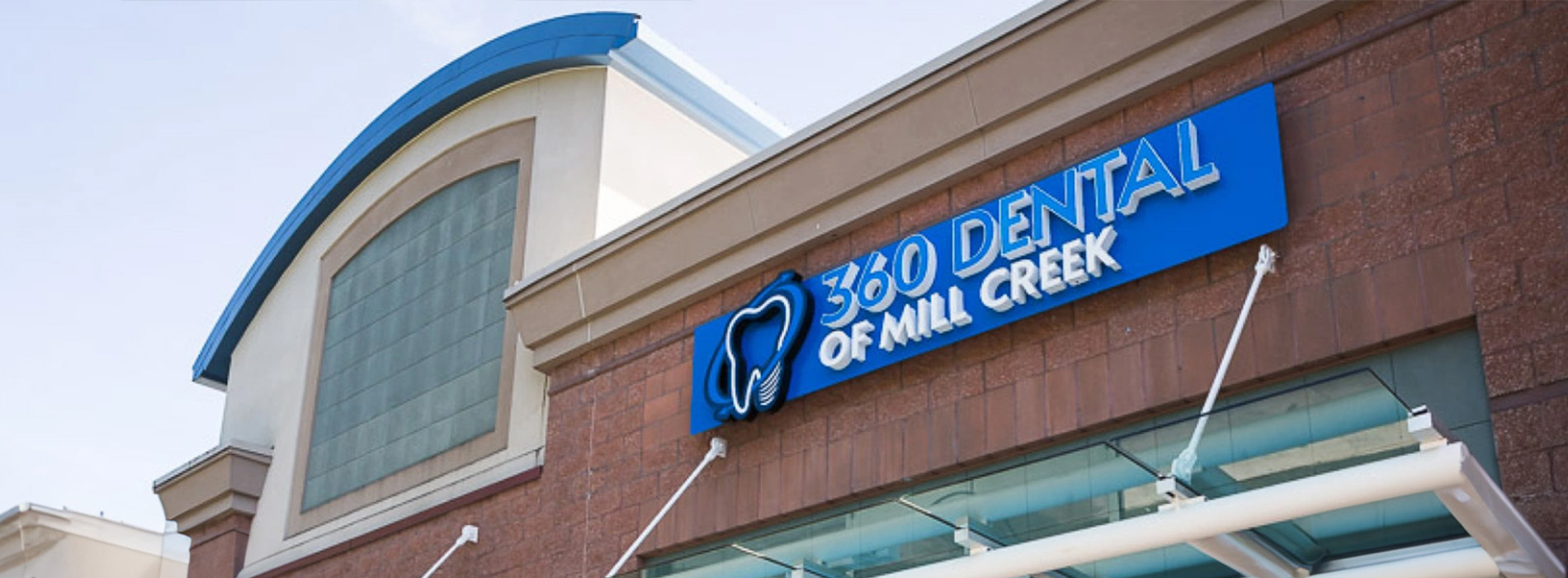 The image shows a building with a blue sign that reads 200 Mill Creek Dental on the front, indicating it s a dental clinic.