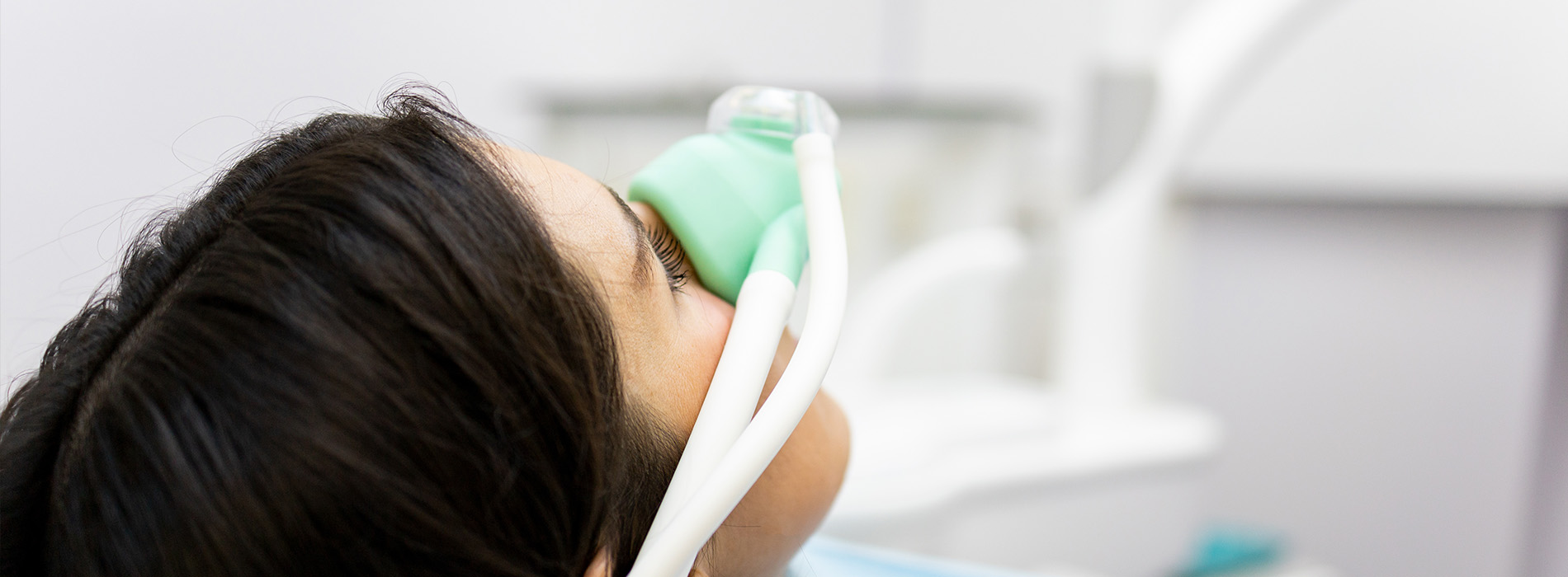 The image shows a close-up view of a person wearing an oxygen mask, with their eyes closed, seemingly asleep or unconscious, against a background that appears to be a medical setting.