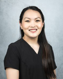 A woman wearing scrubs with long hair, posing for a portrait with a slight smile.