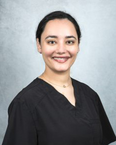 A smiling woman wearing a black dress shirt with a name tag, posing for a professional portrait.