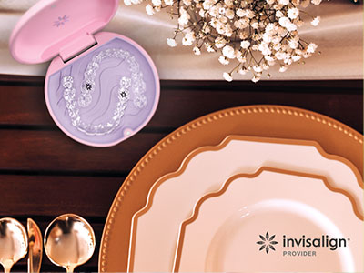 The image shows a collection of items on a dining table, including a pink toothbrush holder with a design on it, a set of plates, a spoon, a vase, and a bottle of nail polish.