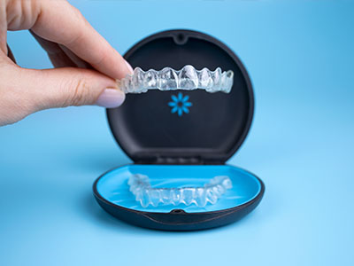 A hand holding a clear plastic tray containing a set of transparent dentures with visible teeth.