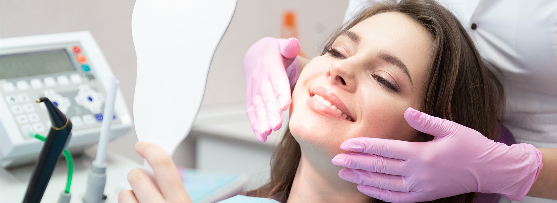 Woman receiving dental treatment with a hygienist using a mirror to show her teeth.
