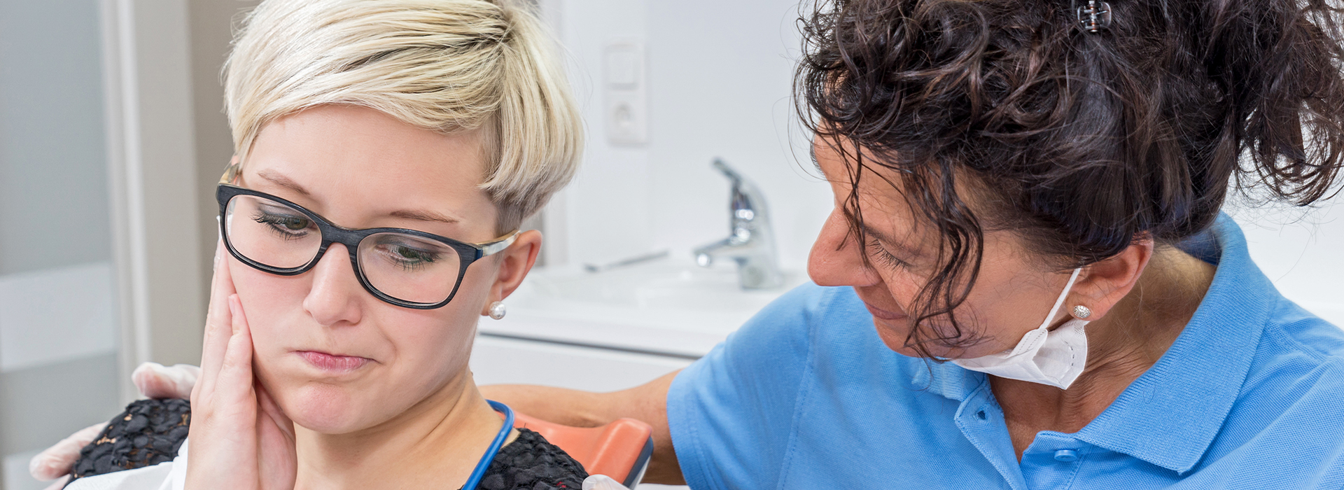 The image shows two individuals in a dental setting a person with glasses is seated while another person, who appears to be a dental professional, stands beside them, both looking at a dental mirror.