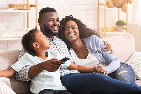 A family of four sitting on a couch, smiling at the camera, with an adult holding a child.