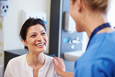 The image shows two individuals in a healthcare setting on the left, there s a smiling woman with dark hair wearing a white top and glasses, standing next to a man who appears to be a medical professional, possibly a dentist, given his attire and the context of the photo.