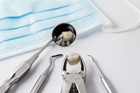 The image shows a collection of dental tools, including a dental mirror, a toothbrush, and a dental pick, placed on a table with blue surgical drapes and gauze in the background.