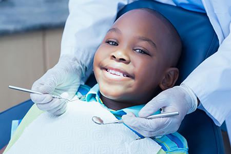A young boy sitting in a dentist s chair with a smile on his face while receiving dental treatment.