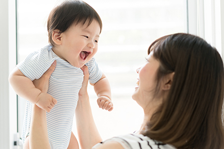 The image shows a woman holding a baby with a joyful expression while looking at them.