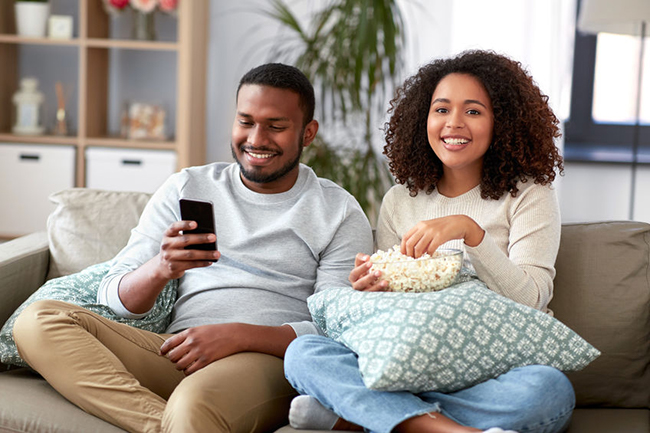 A man and woman sitting on a couch, sharing a moment together while watching something on their phones.